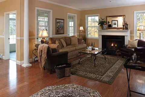 A warmly lit living room with sofas, coffee table, fireplace, and large windows.