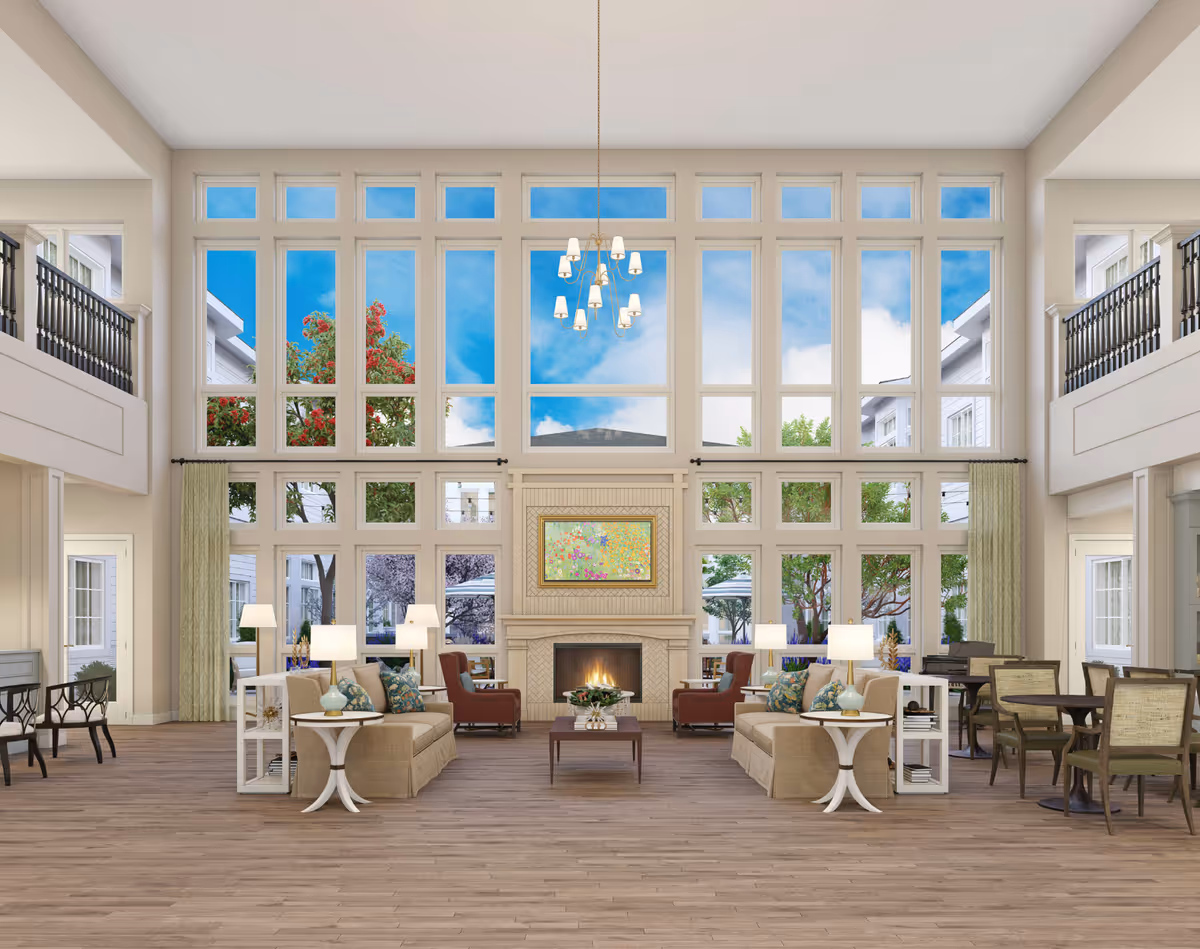 Spacious two-story common lounge with a large wall of windows, central fireplace, seating groups, and dining tables.