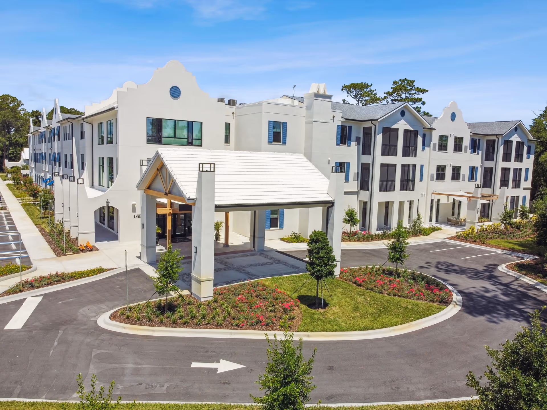 Front entrance and driveway of a three-story white senior living facility with a porte-cochere and landscaped roundabout.