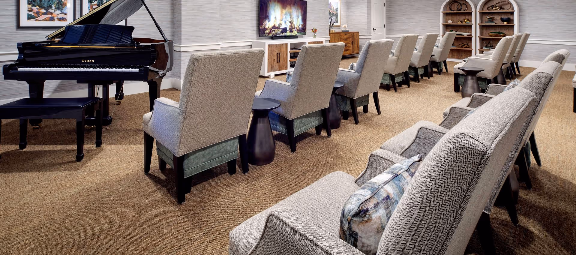 A comfortable common lounge with rows of upholstered chairs facing a television and a grand piano.