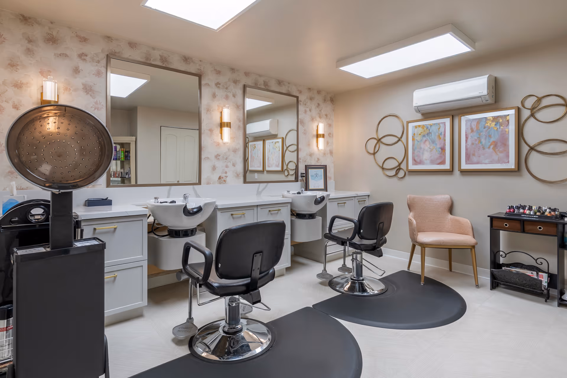 Bright salon-style grooming room with two styling chairs, wash sinks, large mirrors, and a pink accent chair.