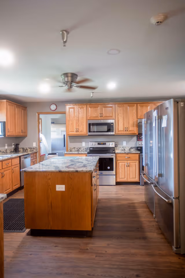 Spacious kitchen with a central island, wooden cabinets, and stainless steel appliances.