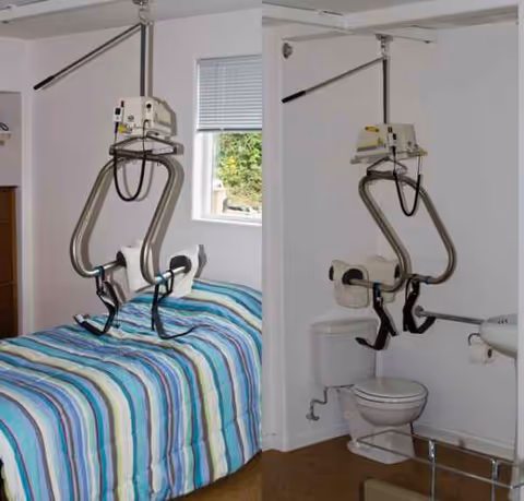 Interior care room with striped bed, ceiling lift, and adjacent bathroom.