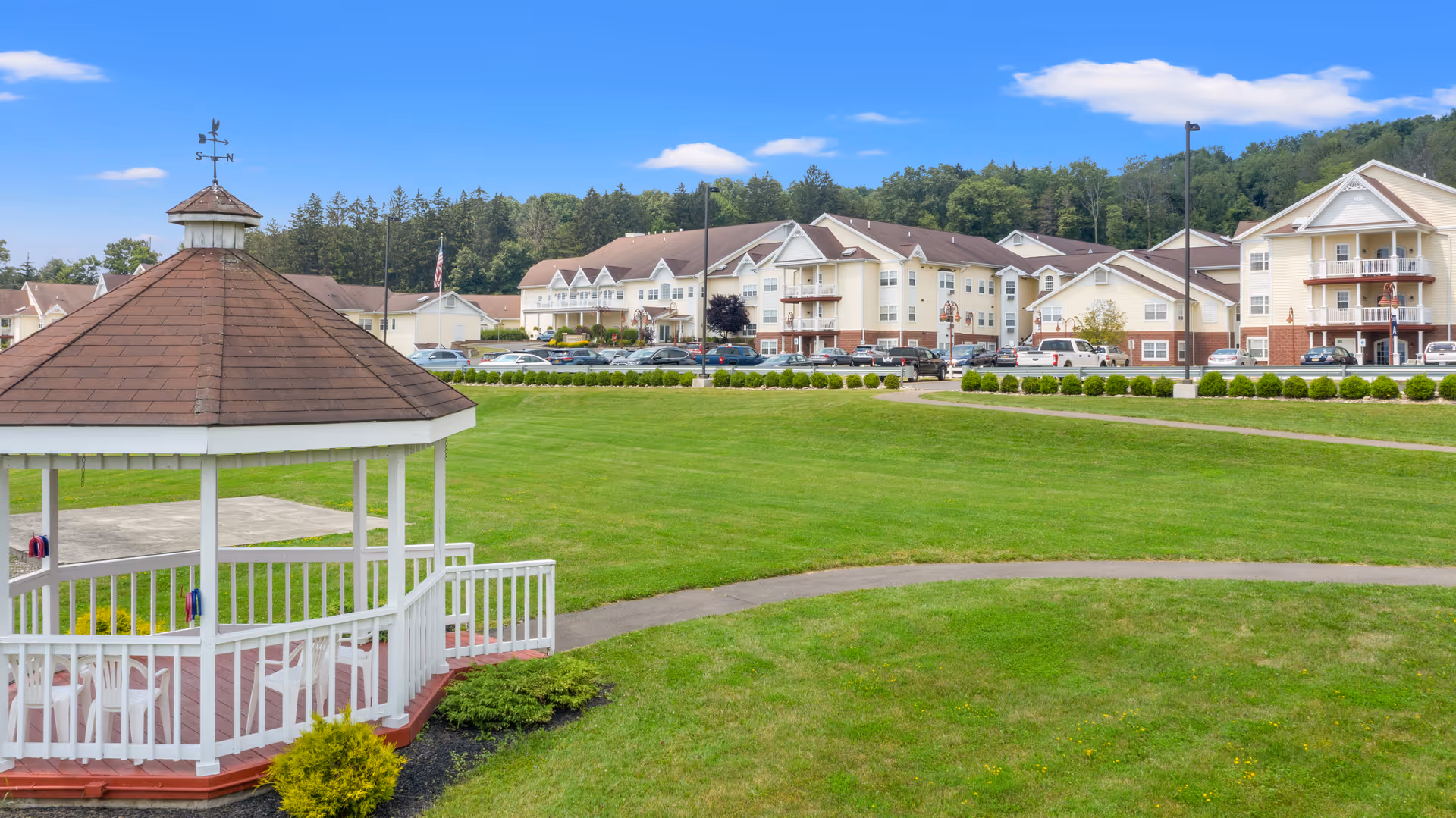 White gazebo on a large green lawn with a multi-story senior living building complex in the background.