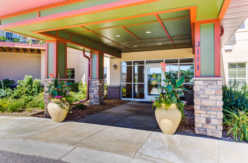 Covered building entrance with glass double doors, stone-clad columns, and two large planters.