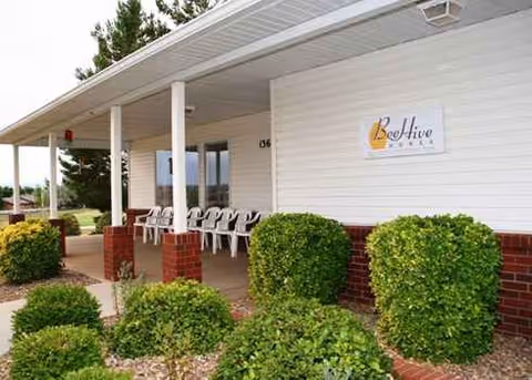 Front of a Beehive Homes facility with a covered porch and trimmed shrubs.