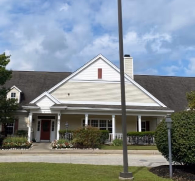 Front exterior of a senior living facility with porch, beige siding, and manicured landscaping.