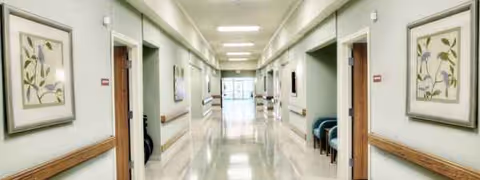 Bright interior hallway of a senior living facility with framed art and benches along walls.