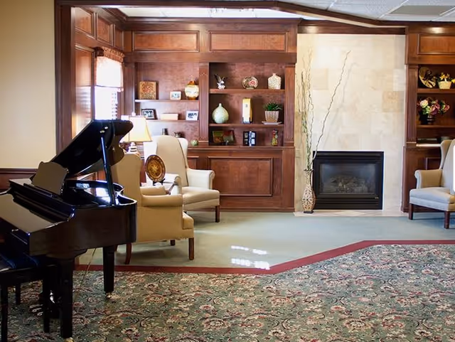 Common living room with a grand piano, upholstered chairs, built-in wood shelving and a fireplace.