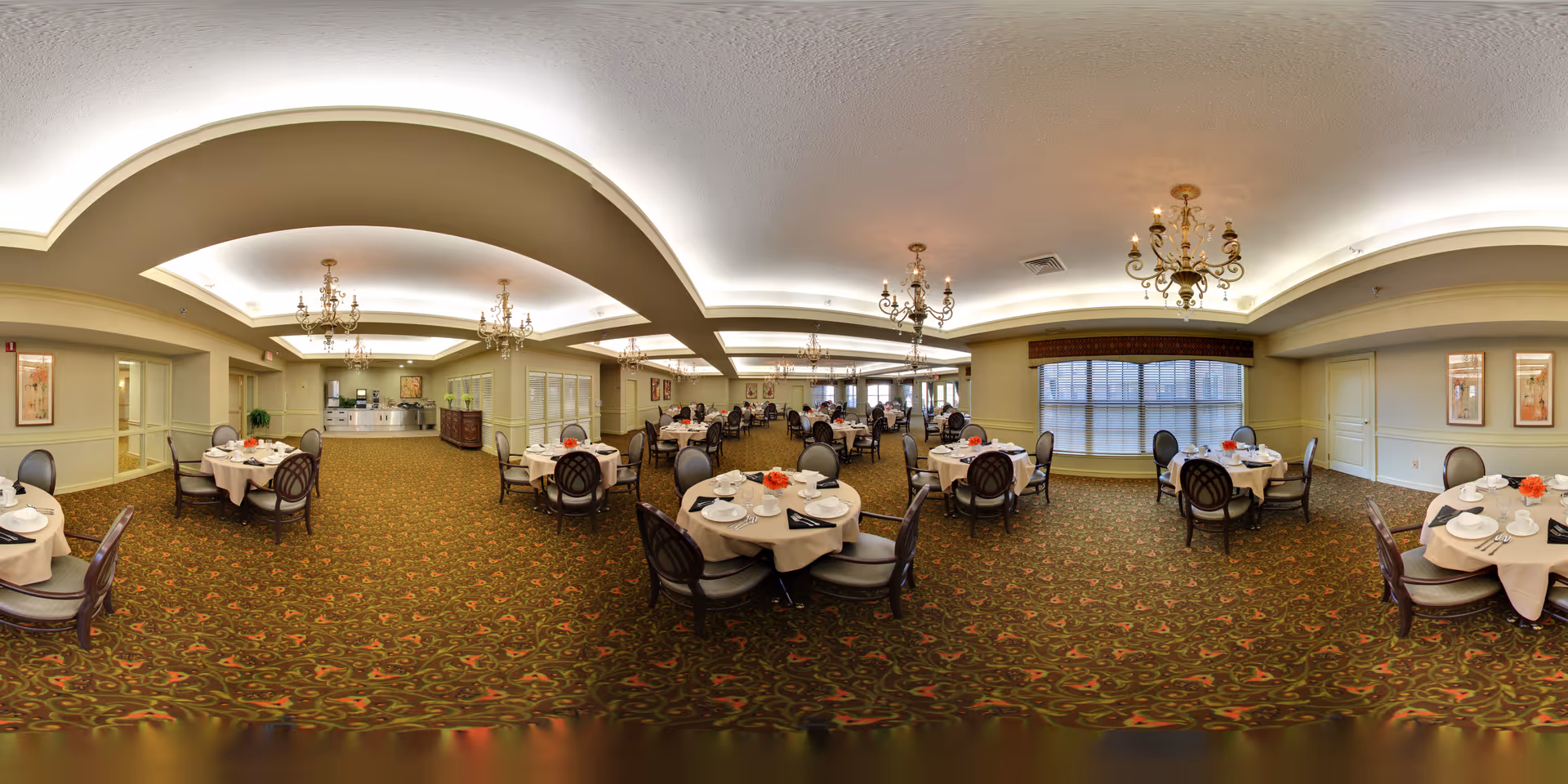 Spacious formal dining room with round tables set for meals, chandeliers, and patterned carpet in a senior living community.