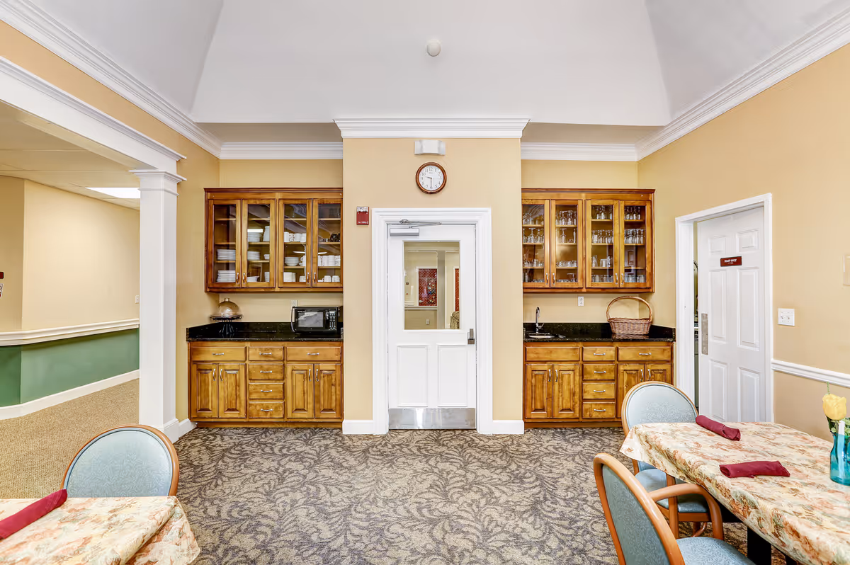 Dining area with wooden built-in cabinets flanking a central door, carpeted floor and tables with chairs in the foreground.