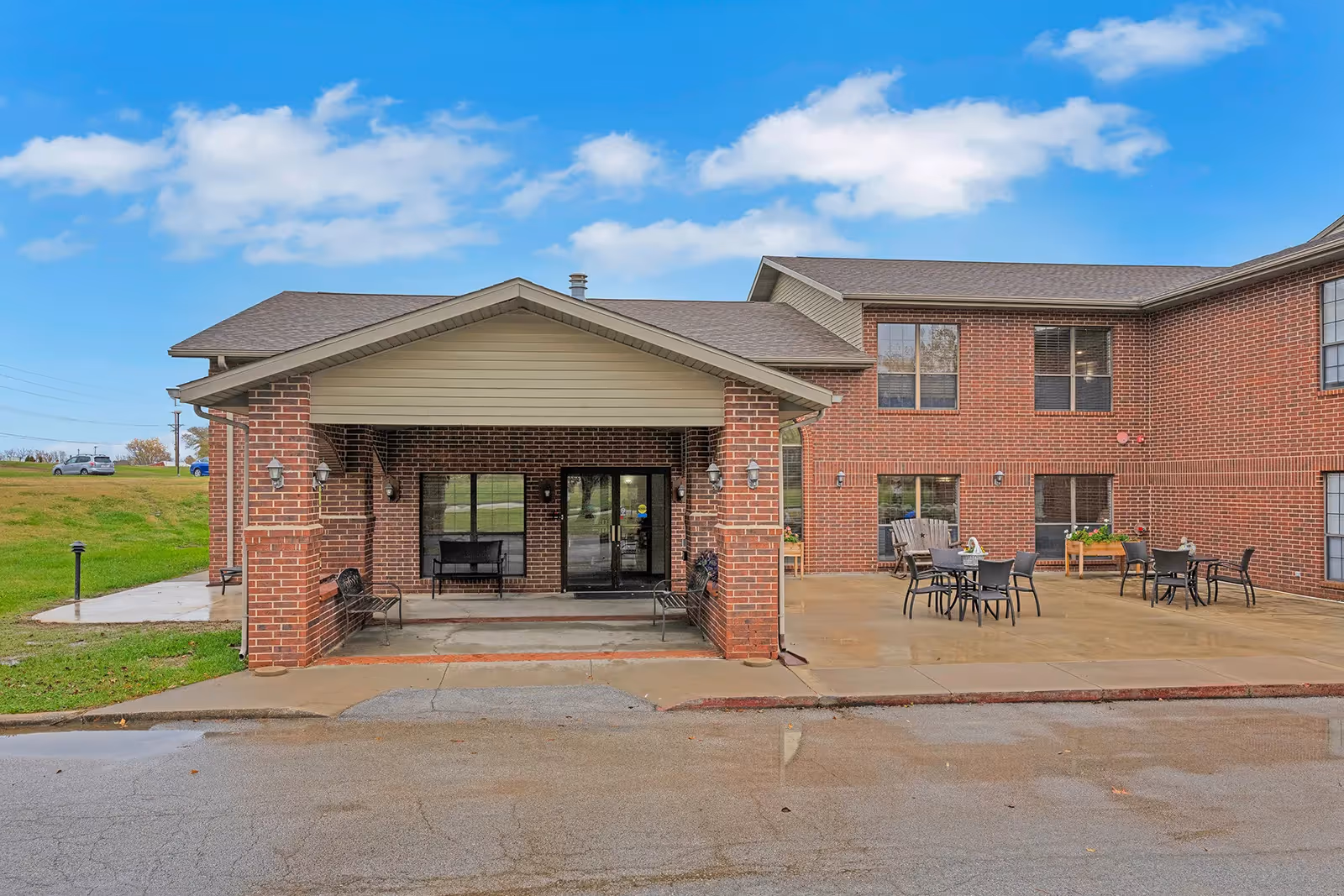 Brick two-story senior living building entrance with a covered porte-cochere and outdoor patio seating.