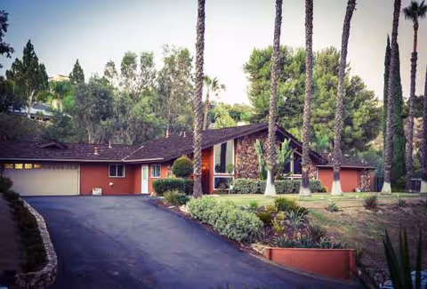Front exterior of a red-brown senior care home with palm trees and driveway.
