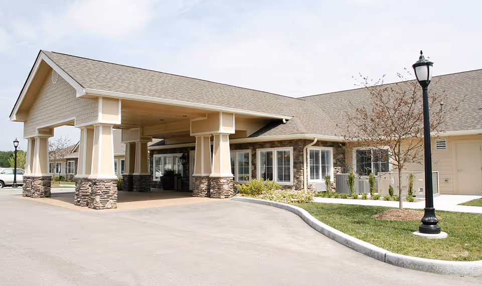 Entrance of a single-story senior living facility with a covered porte-cochère supported by stone-clad columns and a driveway.