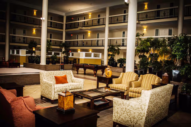 Spacious indoor atrium lounge with sofas, armchairs, coffee tables, potted plants, a pool table, and multi-level balcony walkways.