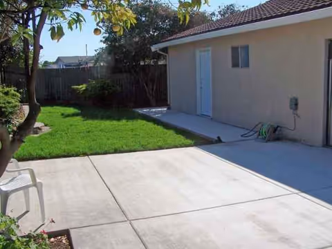Concrete patio with a plastic chair beside a single-story building and green lawn.