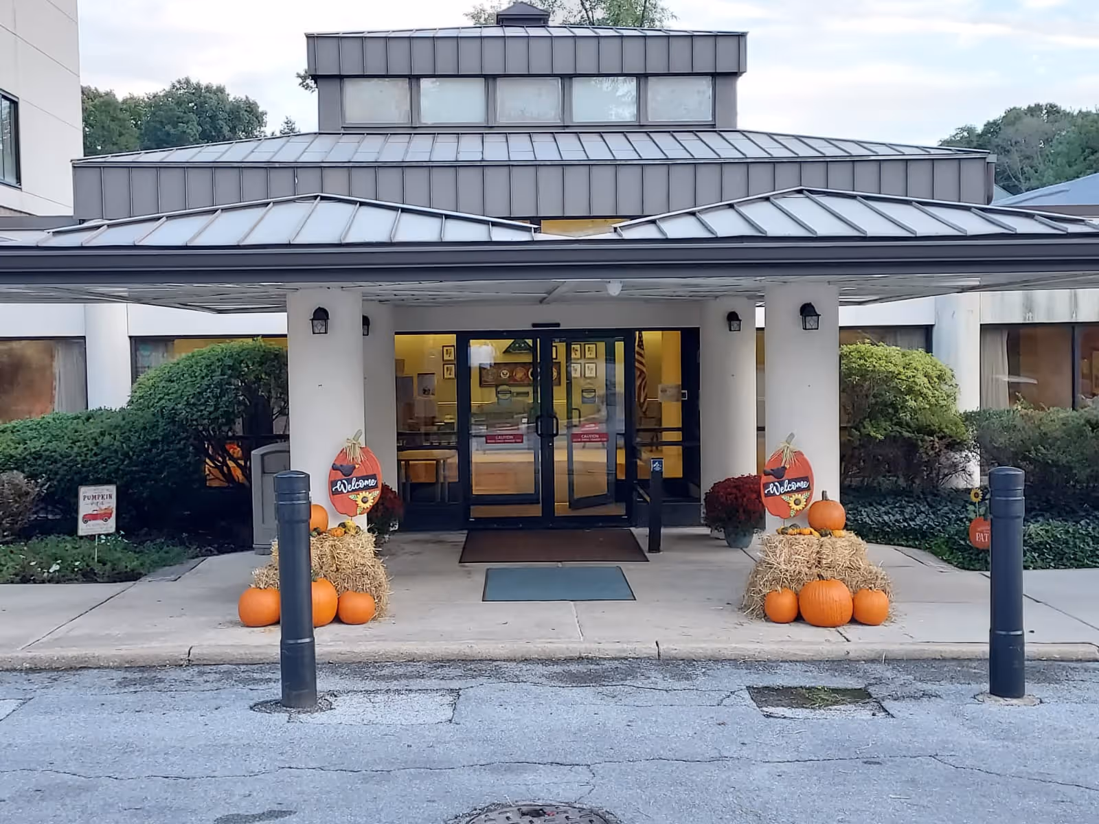 Front entrance of a rehabilitation and healthcare center with glass doors under a covered drop-off area decorated with pumpkins and hay bales.