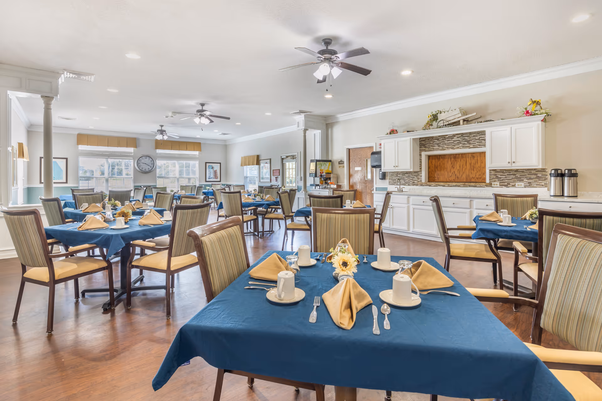 Bright, well-appointed dining room with multiple tables set with blue tablecloths, yellow napkins, and place settings.