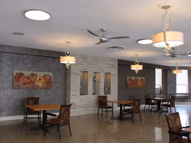 Spacious dining room with several tables and chairs, pendant lights, ceiling fans, and decorative wall art.