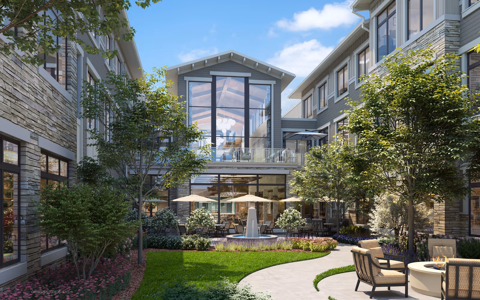 Outdoor courtyard area of The Sheridan At Severna Park featuring a curved walkway, green lawn, trees, and shrubs. There are several seating areas with cushioned chairs around a fire pit and tables with umbrellas near a water fountain. The building surrounding the courtyard has large windows and stone accents under a blue sky with some clouds.
