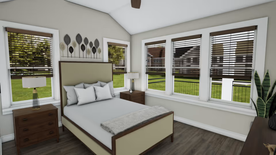 A bright bedroom with a large bed featuring a beige upholstered headboard and white bedding. The room has five windows with brown blinds, allowing natural light to enter and showing a green lawn outside. There are two wooden nightstands with lamps on either side of the bed, a ceiling fan above, and decorative leaf wall art above the headboard. A potted plant and a dresser are visible on the right side of the room.