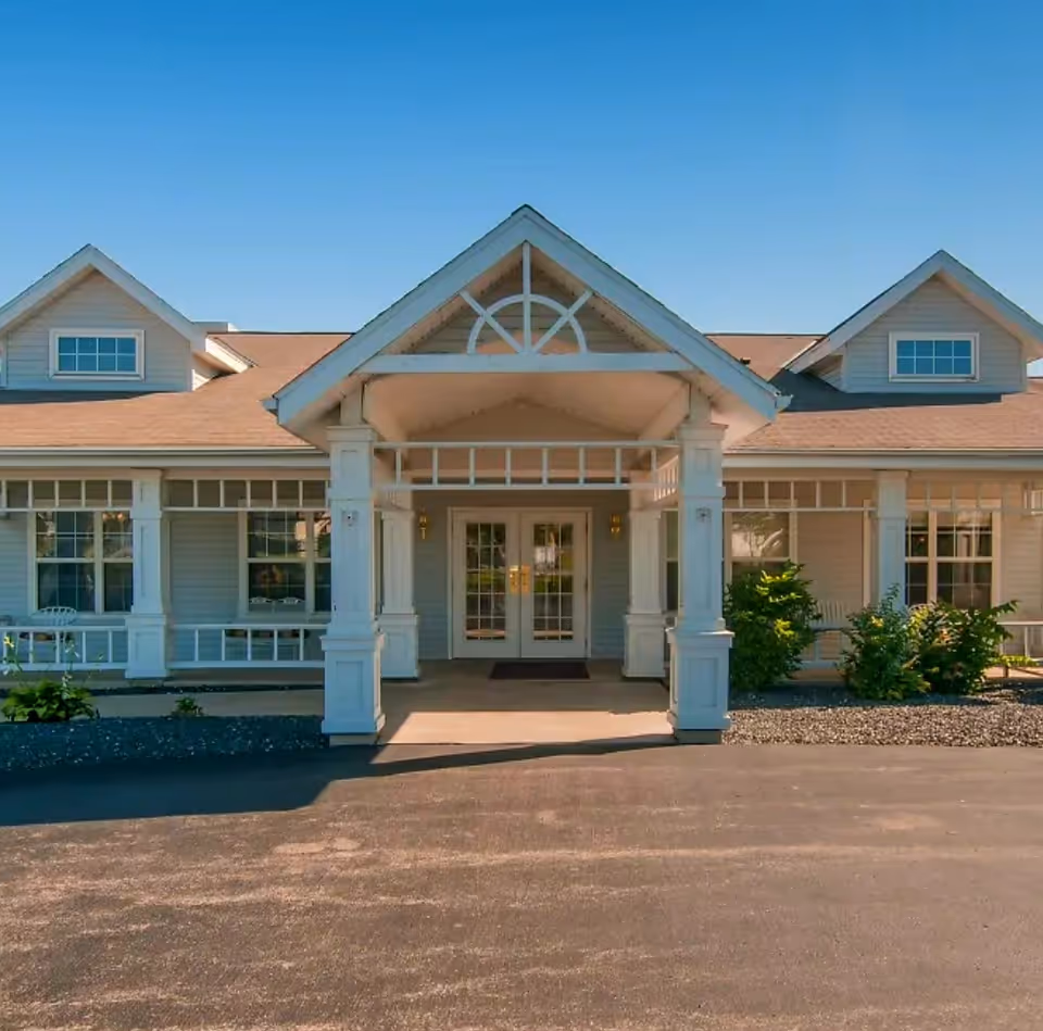 Front exterior view of a single-story building with a covered entrance supported by white columns, large windows, and a clear blue sky above.