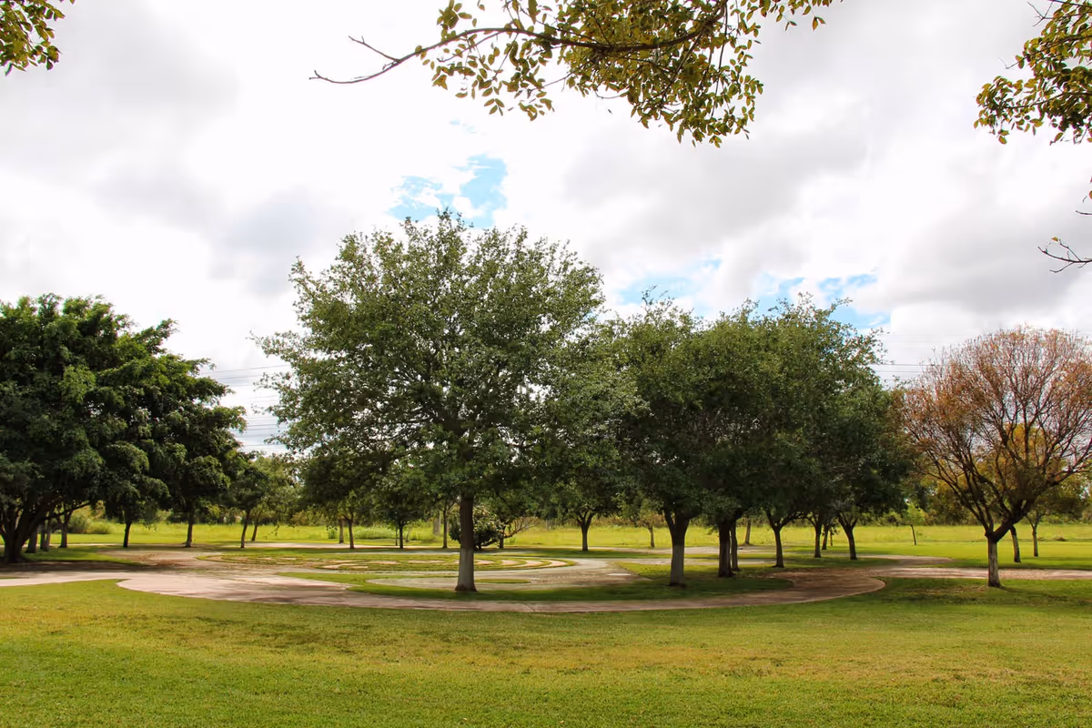 A peaceful outdoor area with a circular paved pathway surrounded by green grass and several trees under a cloudy sky.