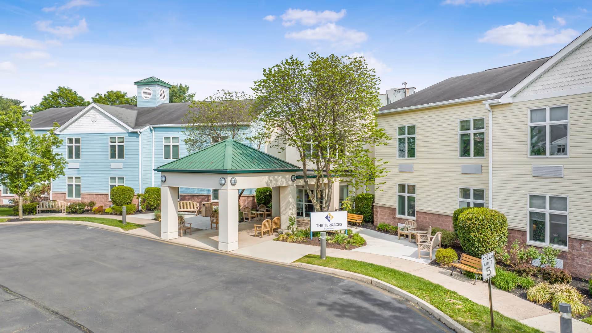 Front entrance of a senior living building labeled "The Terraces" with a covered porte-cochere, benches, and landscaped grounds.