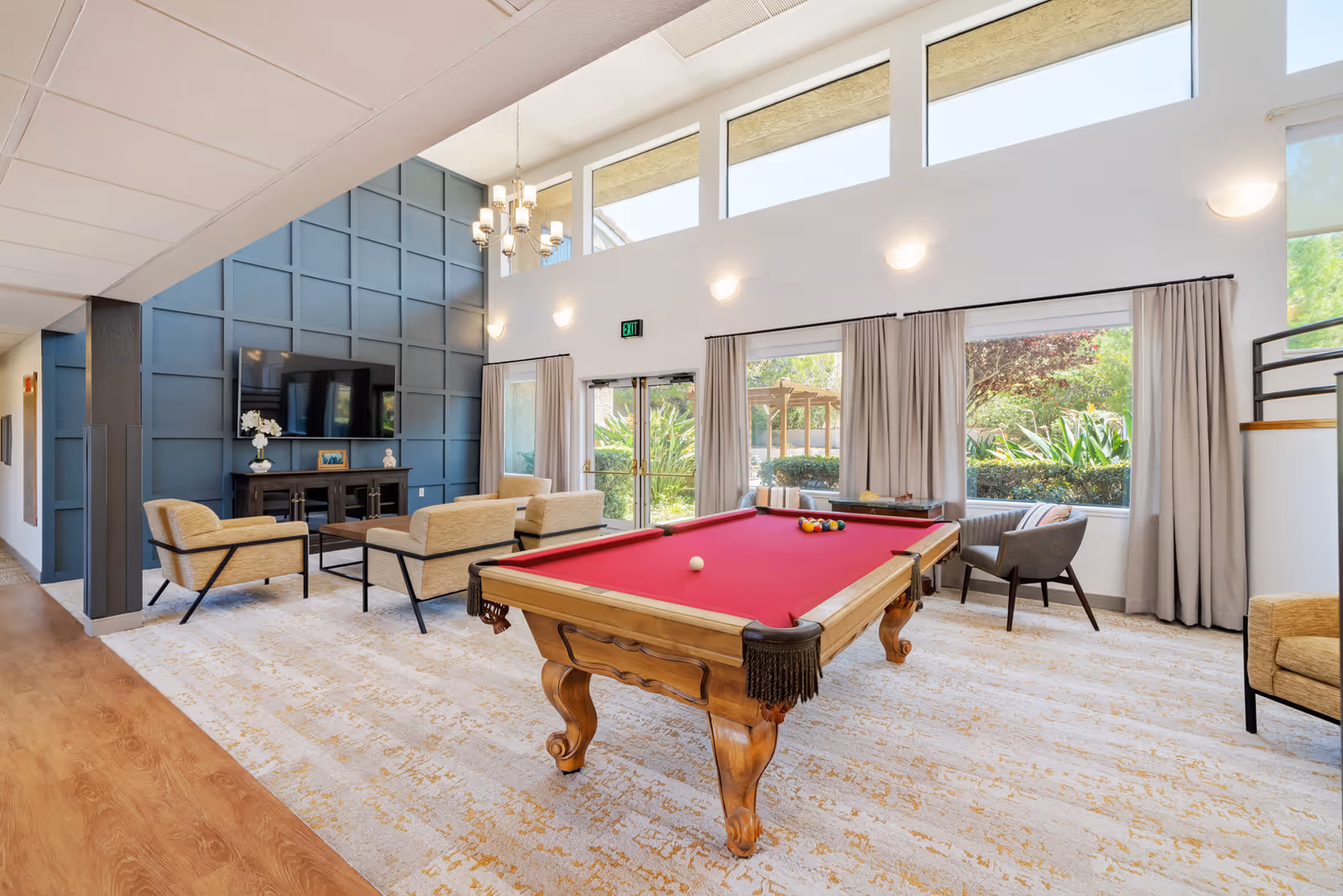 Bright communal lounge with a red-felt pool table, seating area, TV, and large windows.