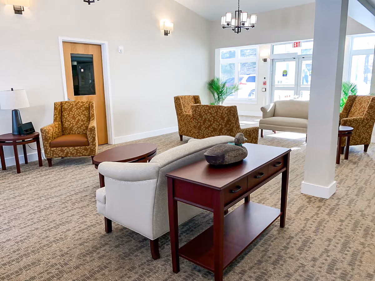 Bright communal lounge with sofas, patterned armchairs, side tables, and large windows.