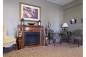 Common area with an electric fireplace mantel, framed painting, upholstered chairs, side tables and decorative vases.