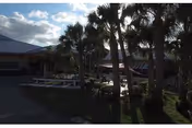Exterior view of a single-story healthcare facility courtyard with palm trees, walkways, and a covered entrance under a partly cloudy sky.