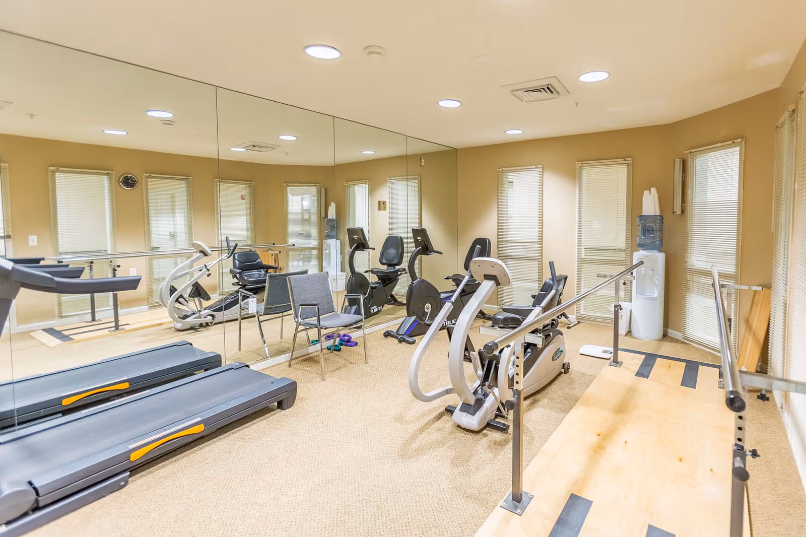 Exercise room with treadmills, stationary bikes, parallel bars, a mirrored wall, chairs, and a water cooler.