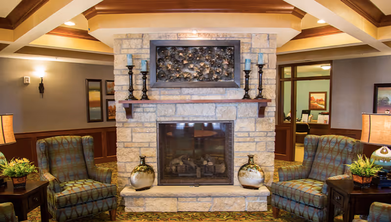 Cozy lounge area with a stone fireplace flanked by patterned armchairs, side tables, and lamps.