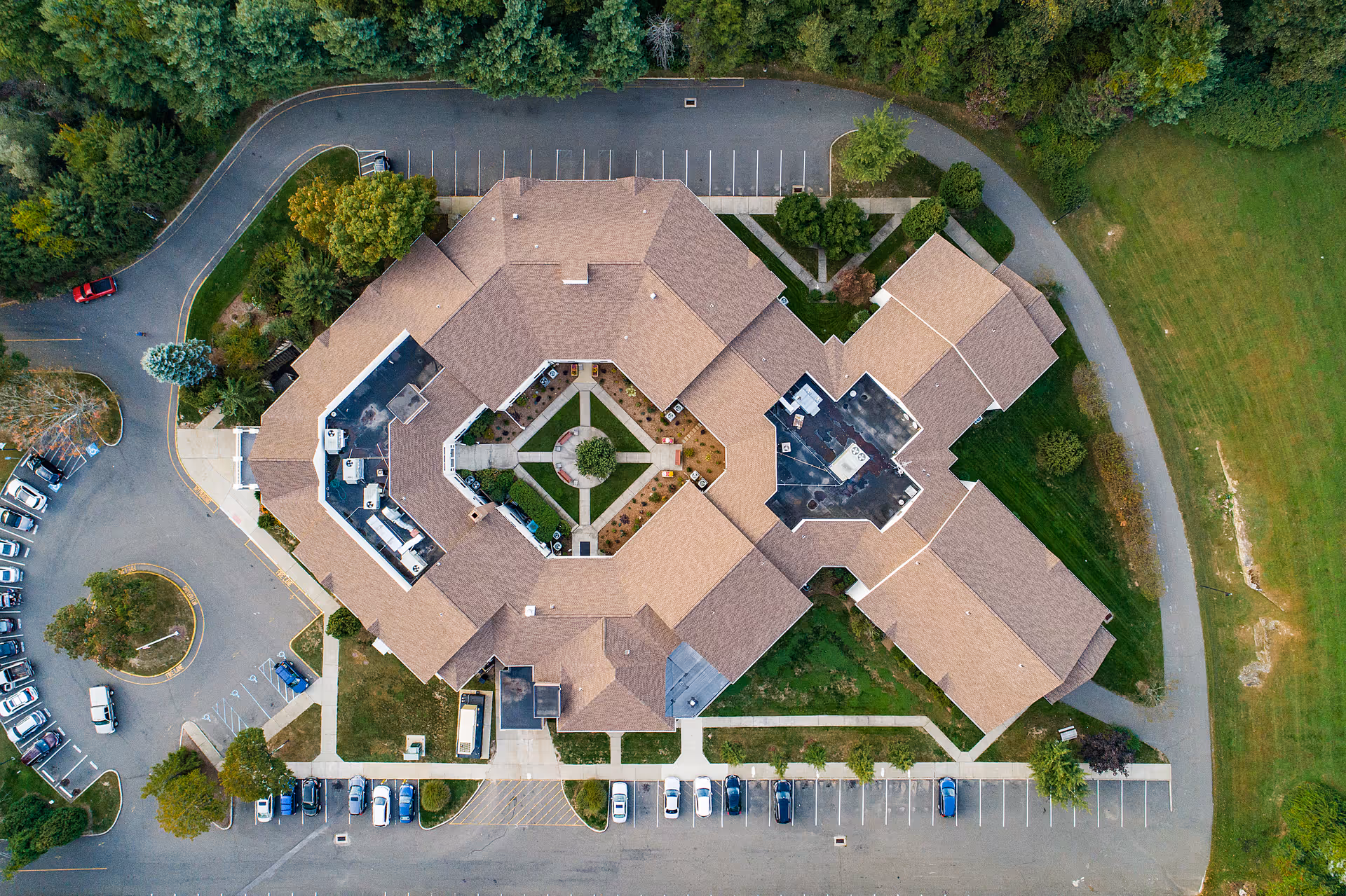 Aerial view of Cambridge Health and Rehabilitation Center showing the building's roof, surrounding parking lots with cars, green lawns, and trees.