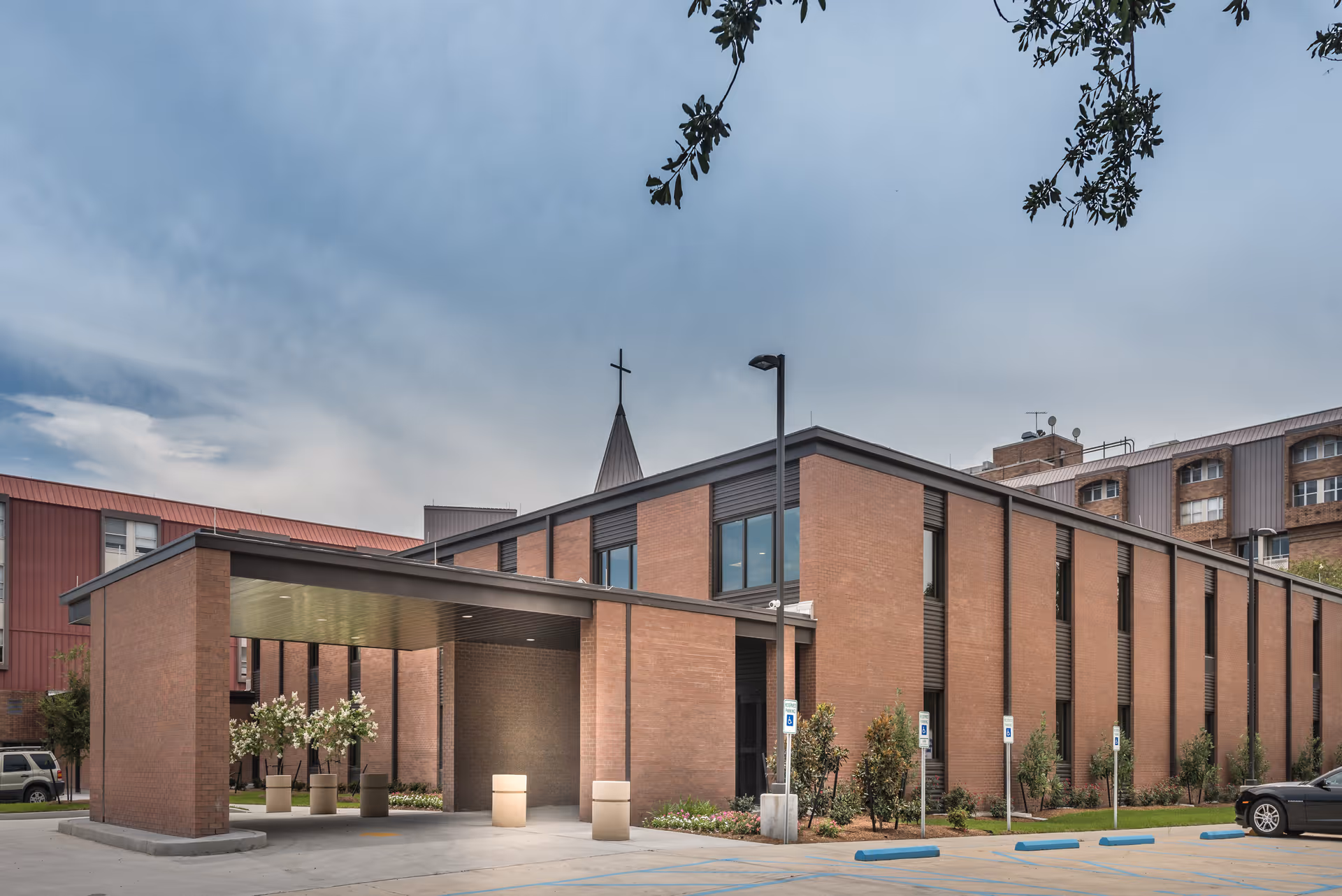 Entrance of a brick assisted living building with a covered drive-through canopy, planters, and adjacent parking spaces.