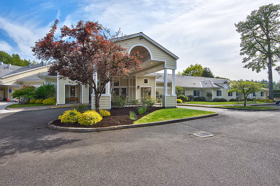 Covered front entrance of an assisted living building with a porte-cochere, landscaped planting island, and a paved driveway.