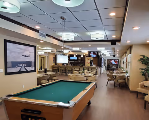 Interior common room with a pool table in the foreground, dining and lounge seating and a bar in the background.