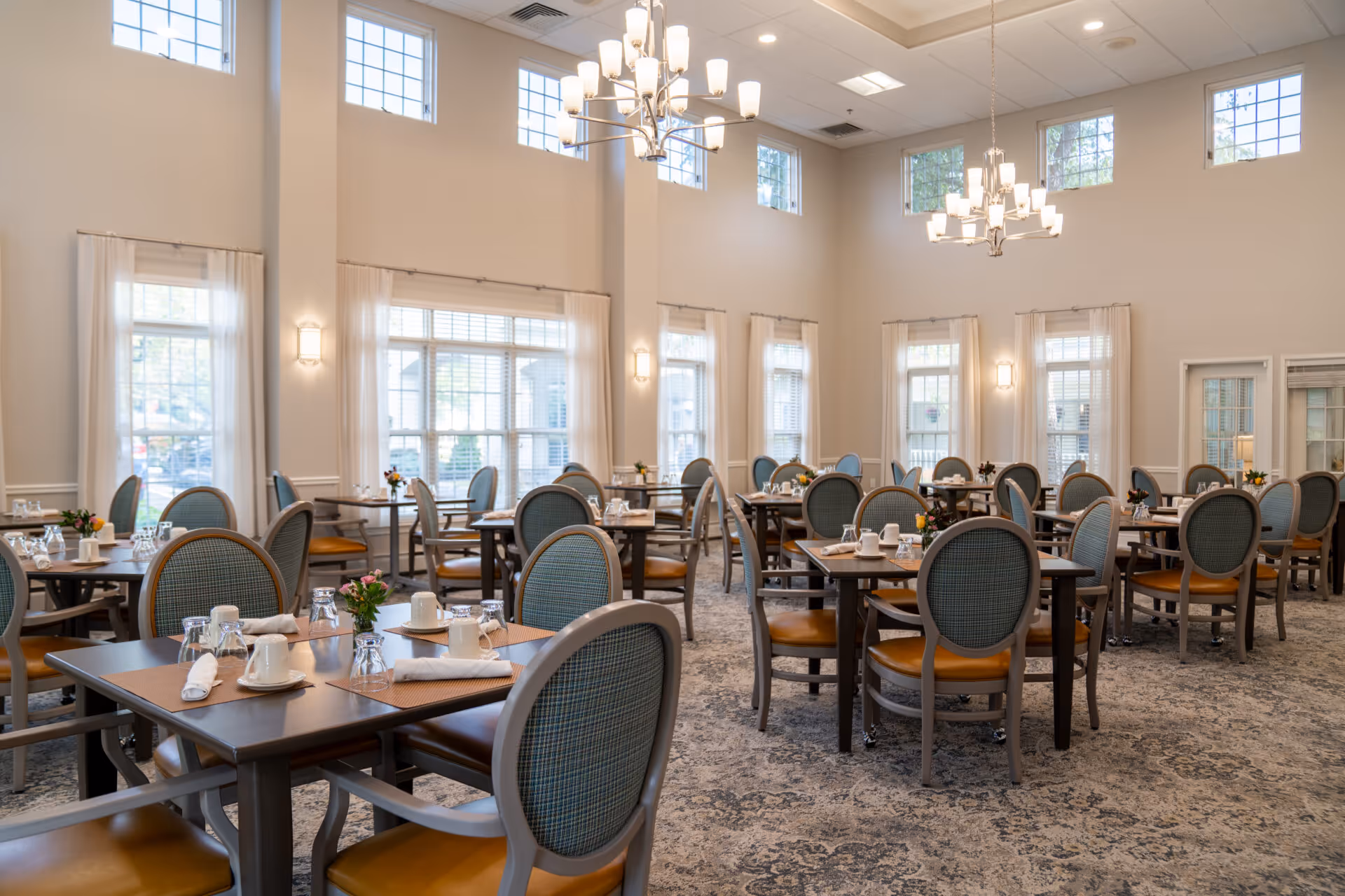 Bright, spacious dining room with set tables, upholstered chairs, and chandeliers.