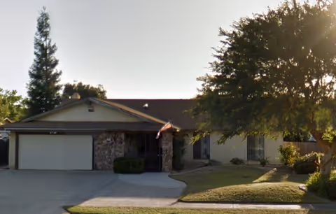 Single-story senior living facility with a two-car garage, stone accents, and front yard.