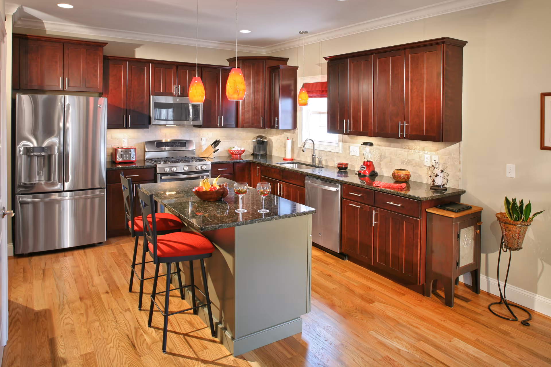 Modern kitchen with dark wood cabinets, stainless steel appliances, an island with red-cushioned stools and pendant lights.