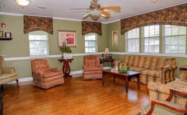 Interior living room at Nixon Assisted Living with sofa, armchairs, coffee table, and large windows.