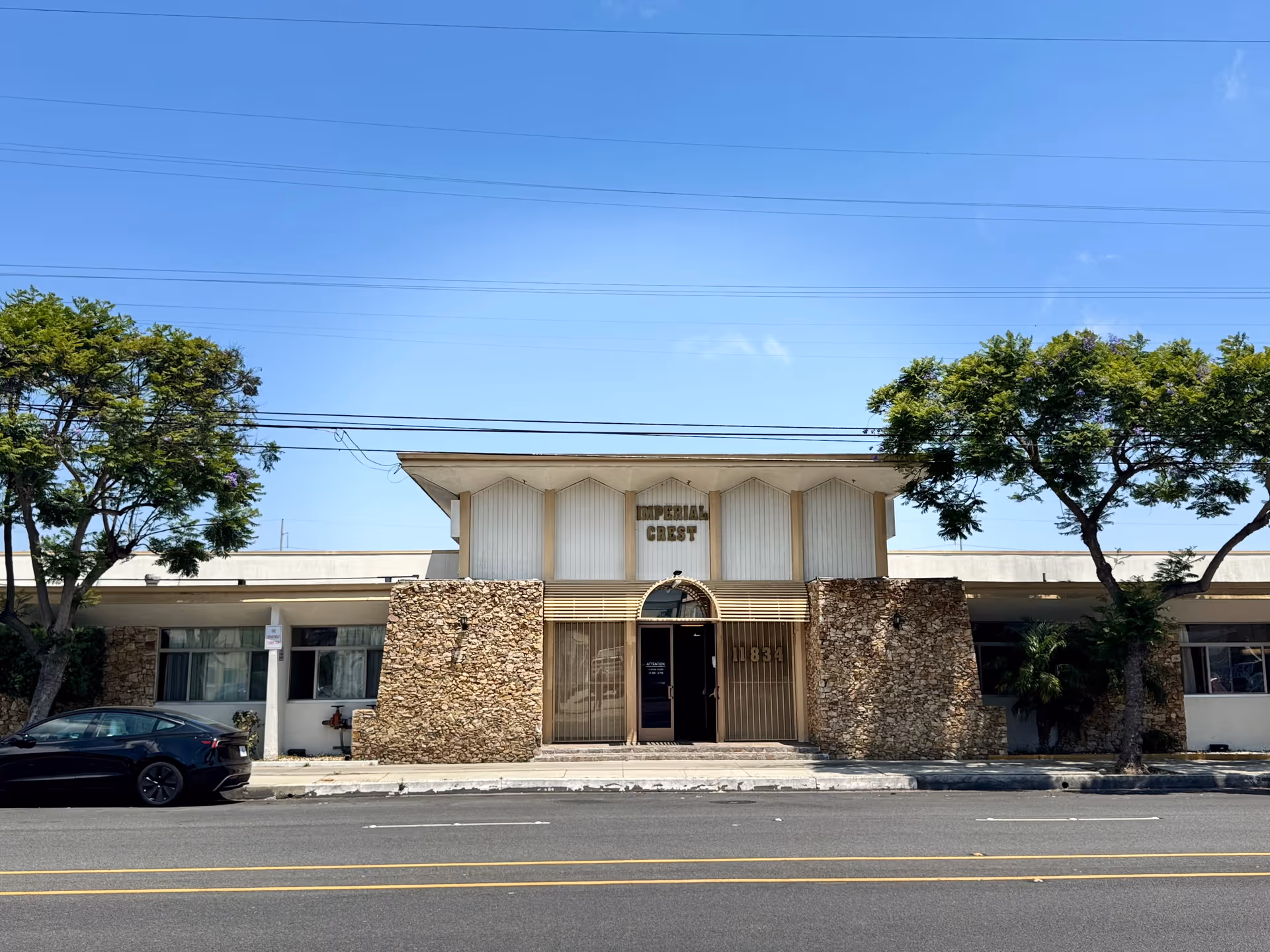 Front facade of the Imperial Crest Healthcare Center building with stone accent walls, a central arched entrance and trees along the sidewalk.