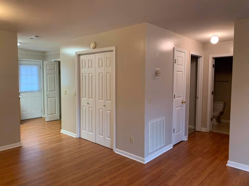 Empty interior space with wood floors, white bi-fold closet doors, multiple doorways, and a visible bathroom.