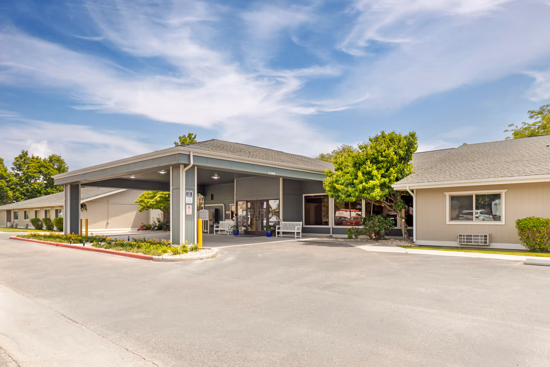 Exterior view of Brookdale Ontario senior living facility entrance with a covered drop-off area, benches, and surrounding greenery under a partly cloudy sky.