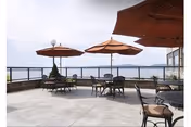 Rooftop patio with tables, chairs, and large umbrellas overlooking a waterfront view.