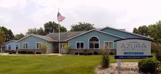 Single-story blue senior living building with flagpole, lawn, and arched window.