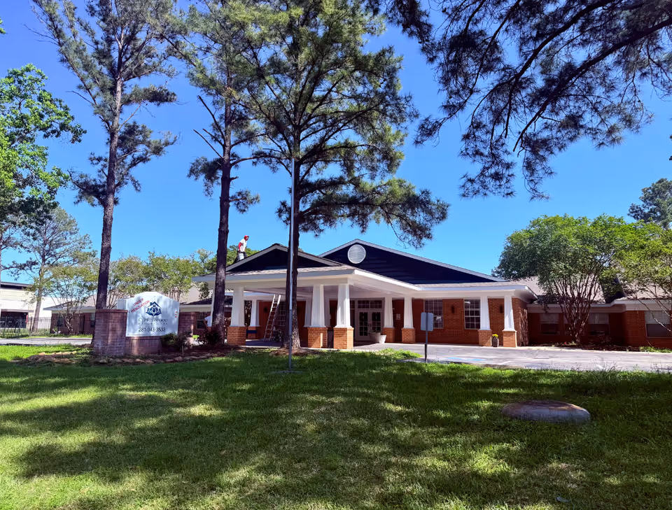 Front exterior of a single-story brick memory care building with a covered columned entrance and trees on a sunny day.
