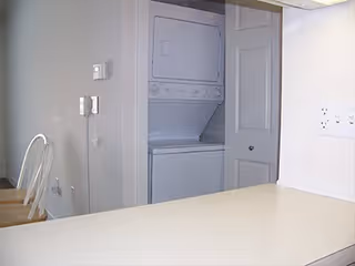 Kitchen countertop with chairs and a closet containing a stacked washer and dryer.