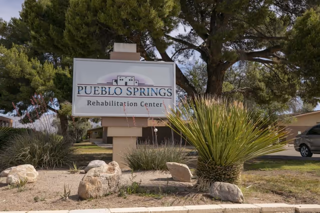 Outdoor photo of the Pueblo Springs Rehabilitation Center sign with landscaping and trees in front of the building.